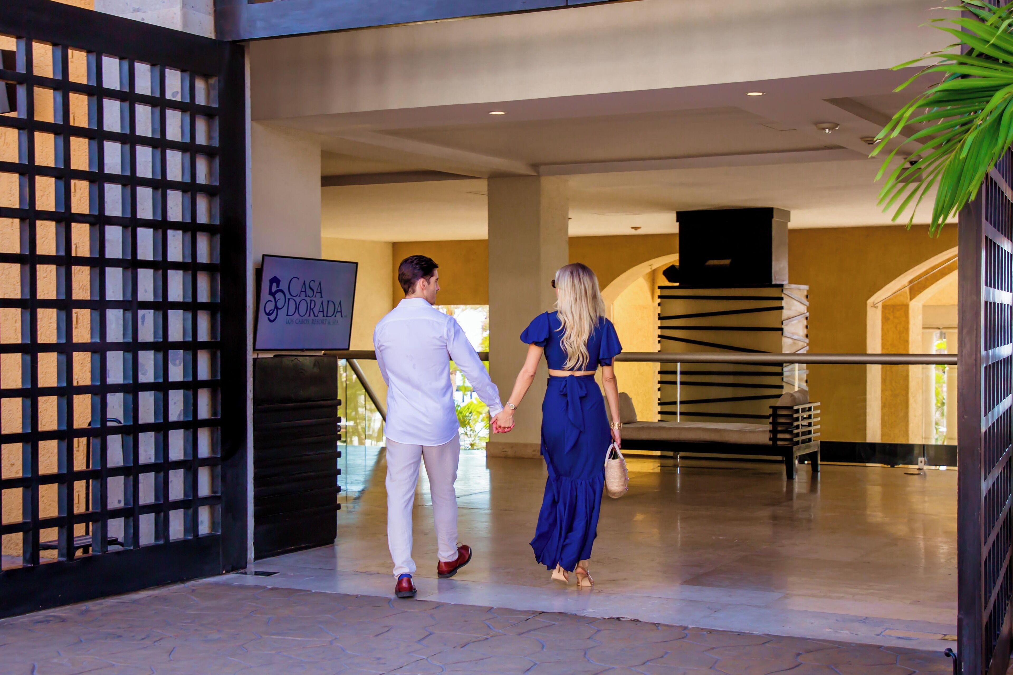 A couple walking through the entrance of a hotel with a sign that reads "Casa Dorada."