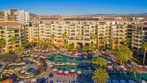Un hotel con varios pisos, una piscina central y palmeras aledañas.