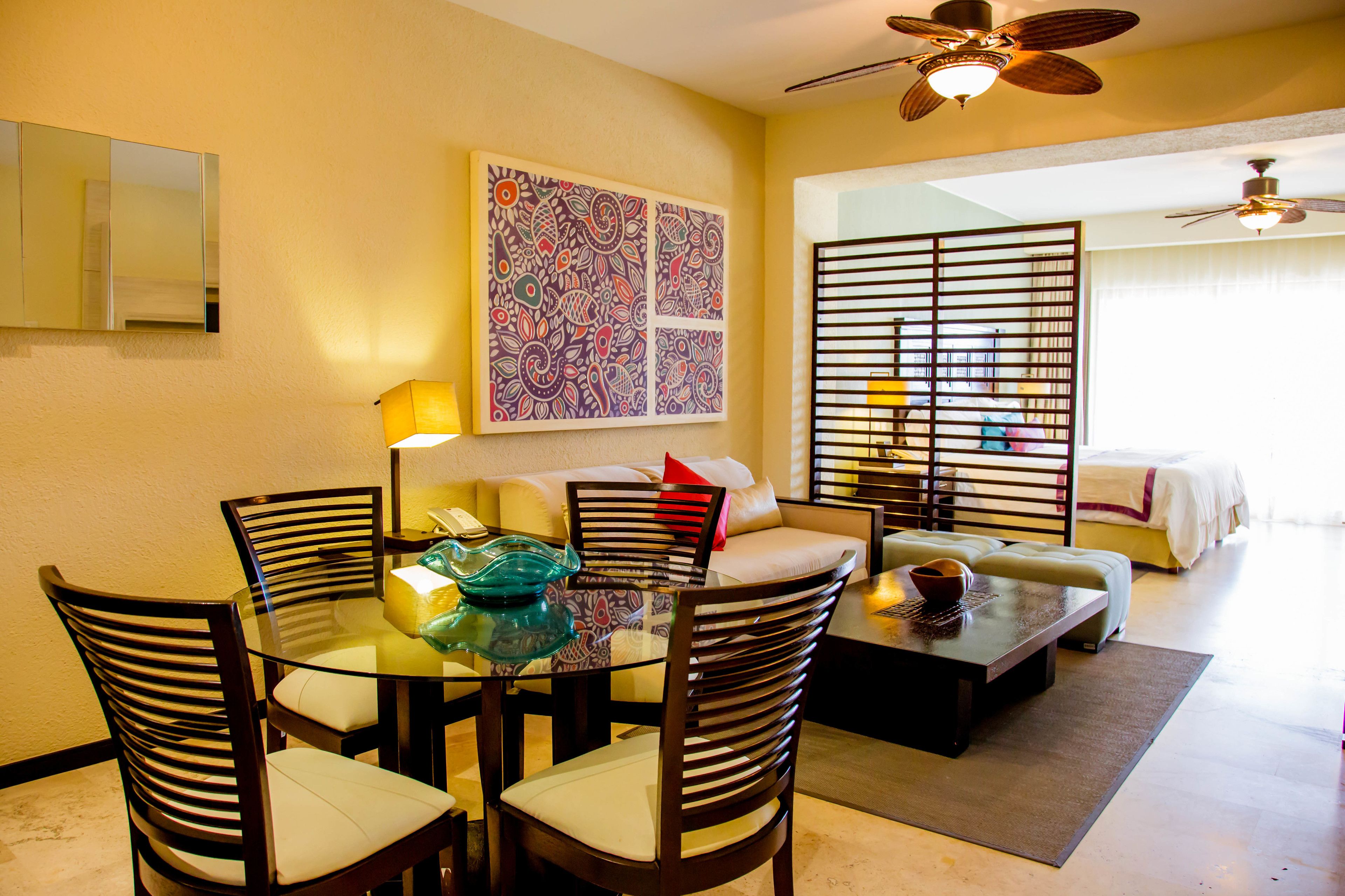 A hotel room with a dining area, a sofa, a bed, and a large window.