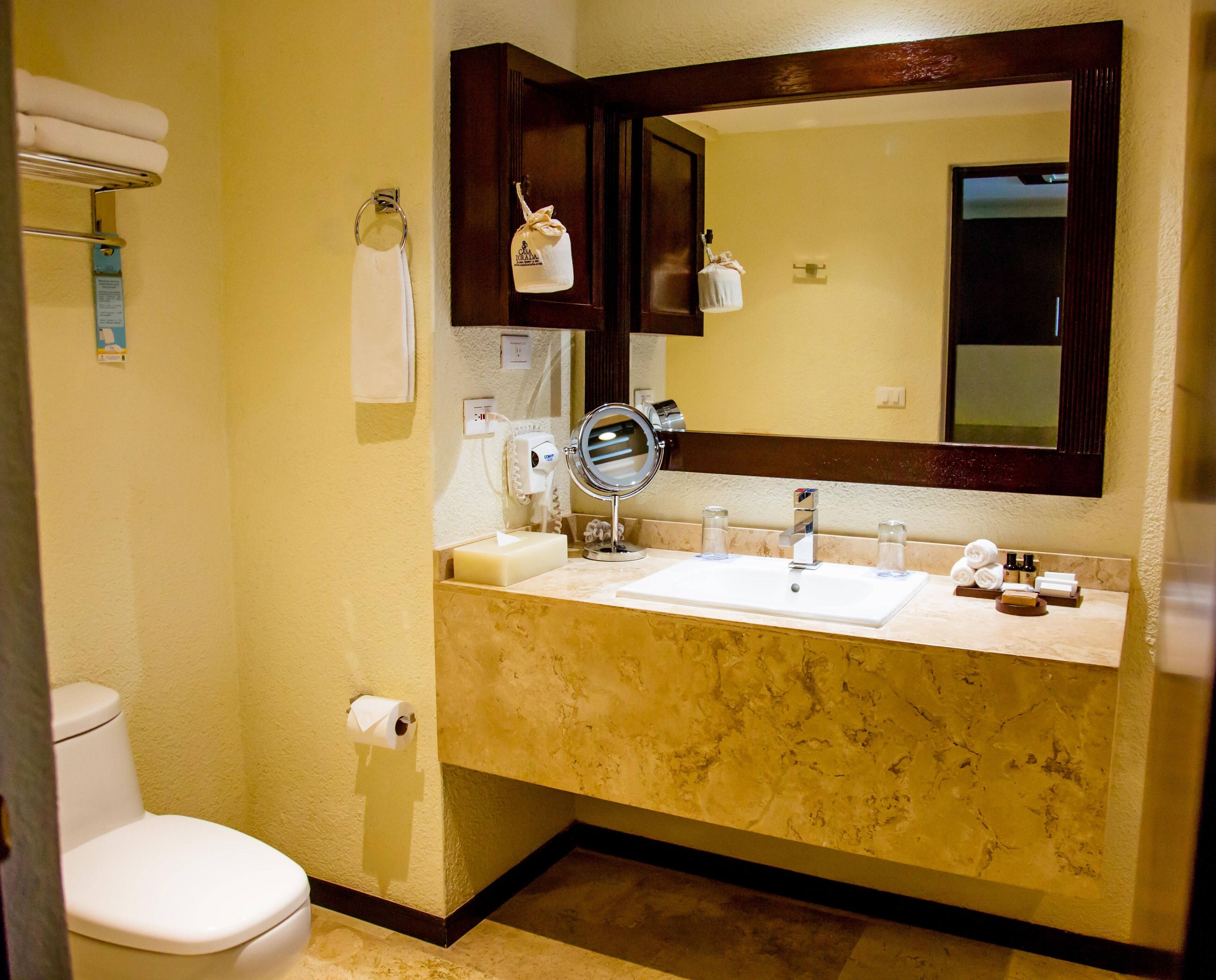 Une salle de bain équipée d’un WC, d’un lavabo, d’un miroir, d’un porte-serviettes et d’un sèche-mains.