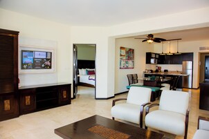 Una sala de estar moderna con televisor de pantalla plana, un comedor con mesa y sillas, una cocina con armarios oscuros y electrodomésticos de acero inoxidable, y un ventilador de techo.