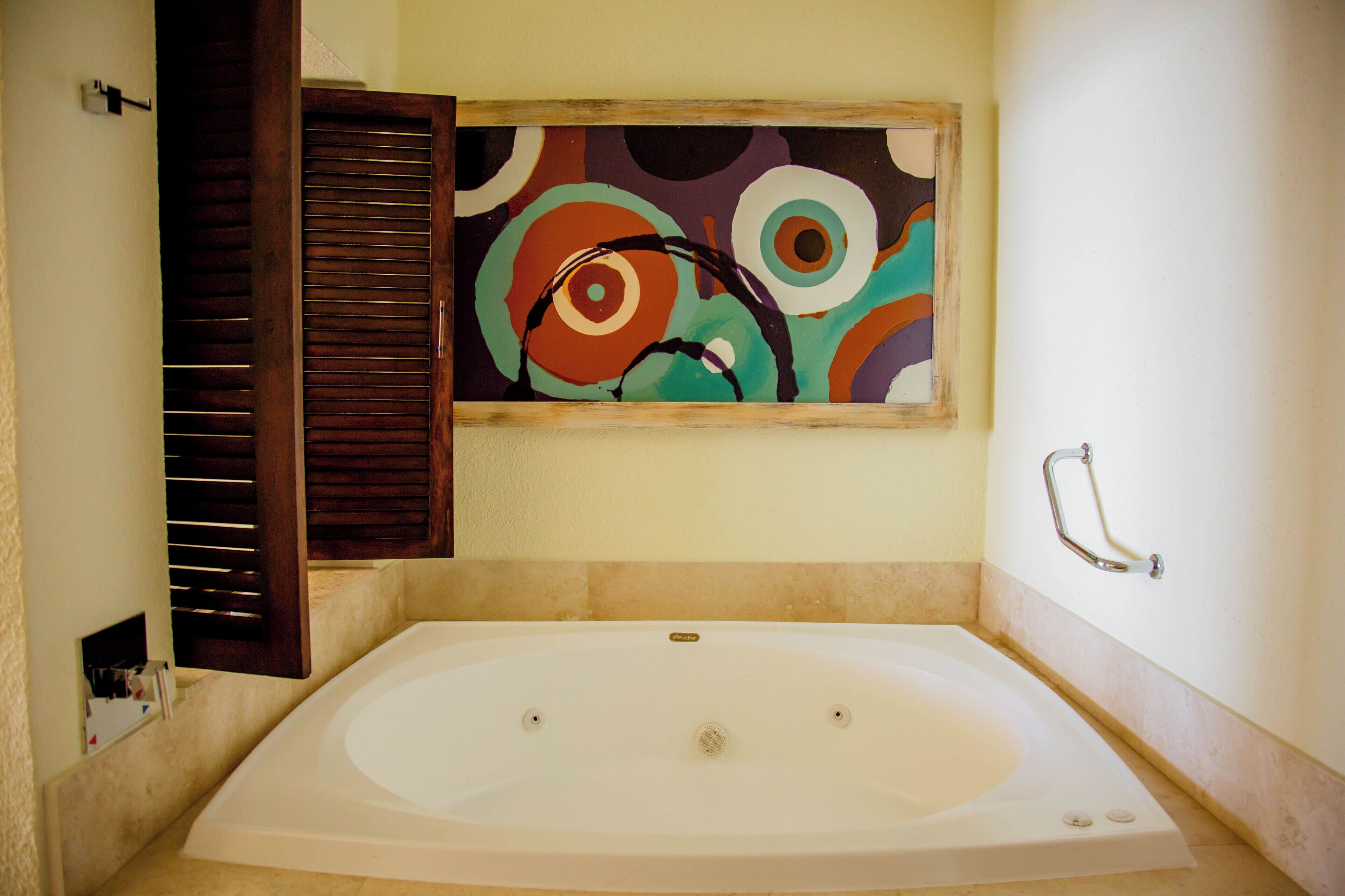 Une salle de bain avec une grande baignoire, une porte en bois et un tableau abstrait aux couleurs vives accroché au mur.
