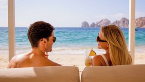 Una pareja sentada en sillas junto a la playa, mirando al océano, con una bebida en la mano.