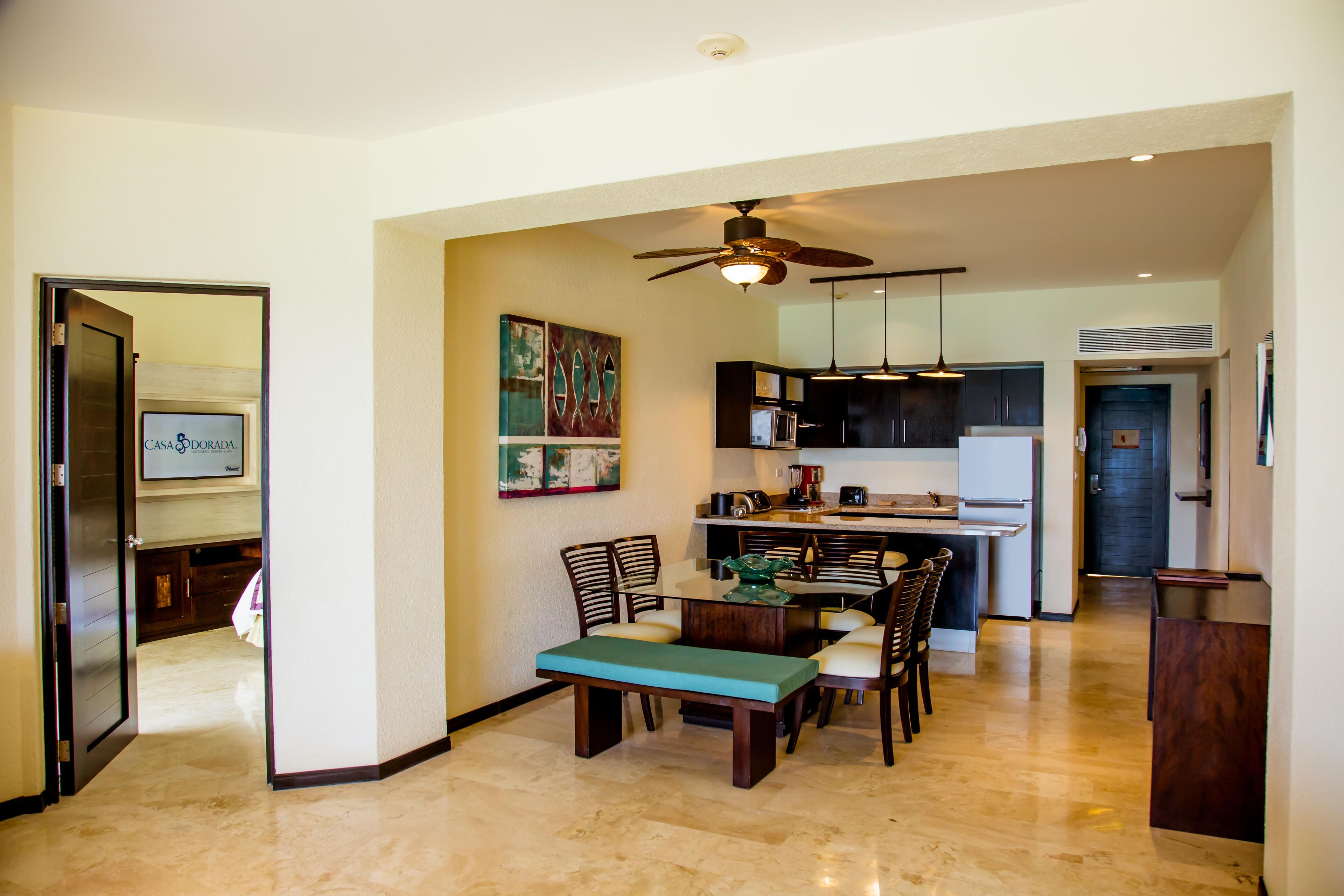 A modern kitchen with dark cabinets, a dining area with a bench and chairs, and a ceiling fan.