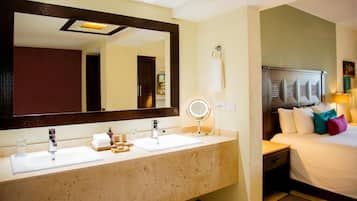 Un baño de hotel con dos lavamanos, un espejo grande, un tocador y una cama con almohadas.
