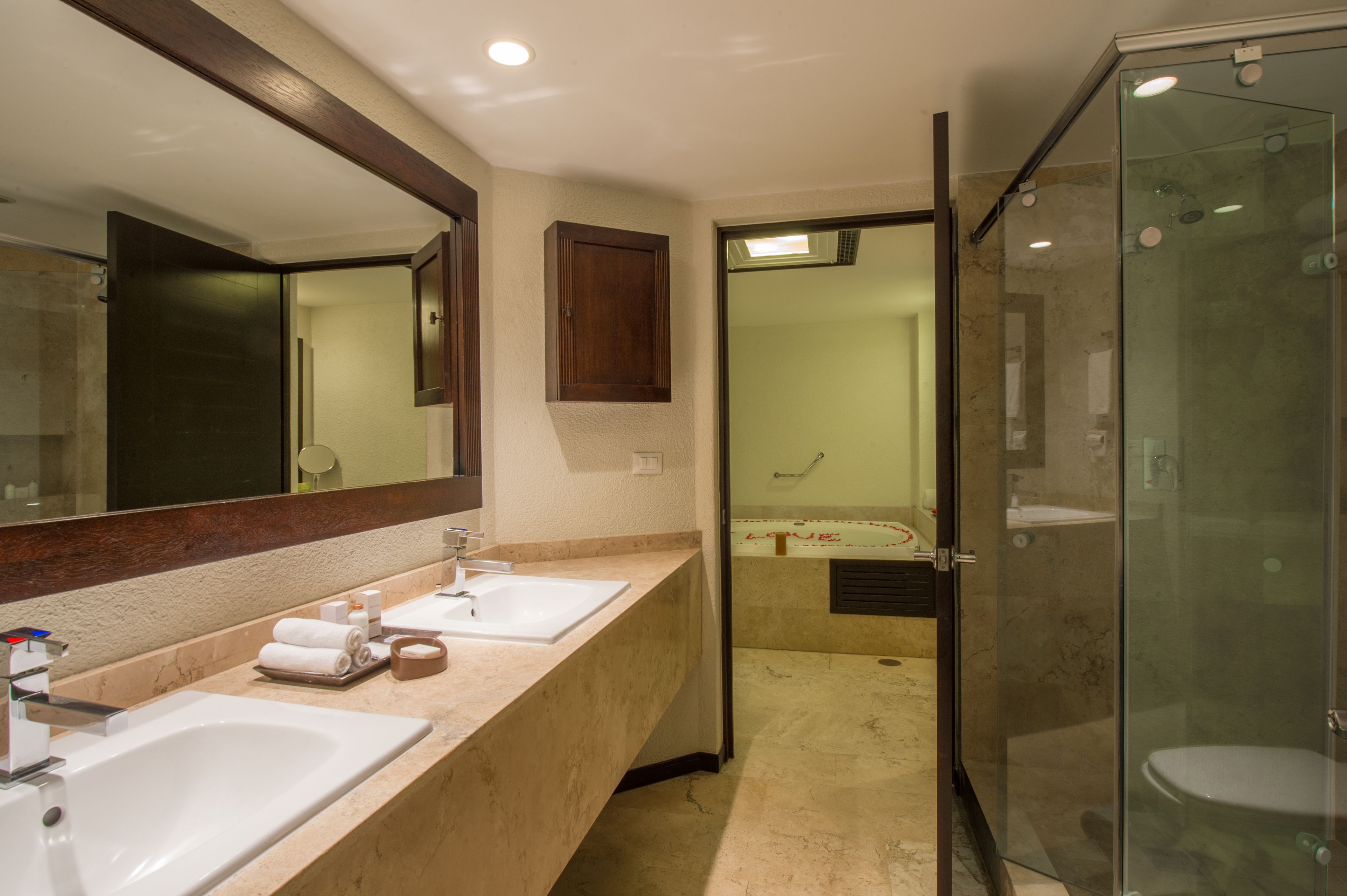 A hotel bathroom with two sinks, a large mirror, and a glass-enclosed shower area.