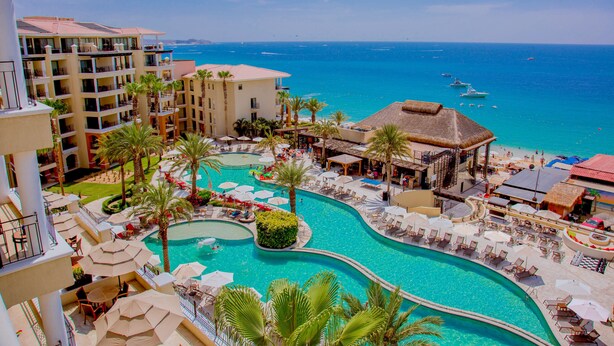 Un resort con una amplia piscina, varios balcones y vista al océano.