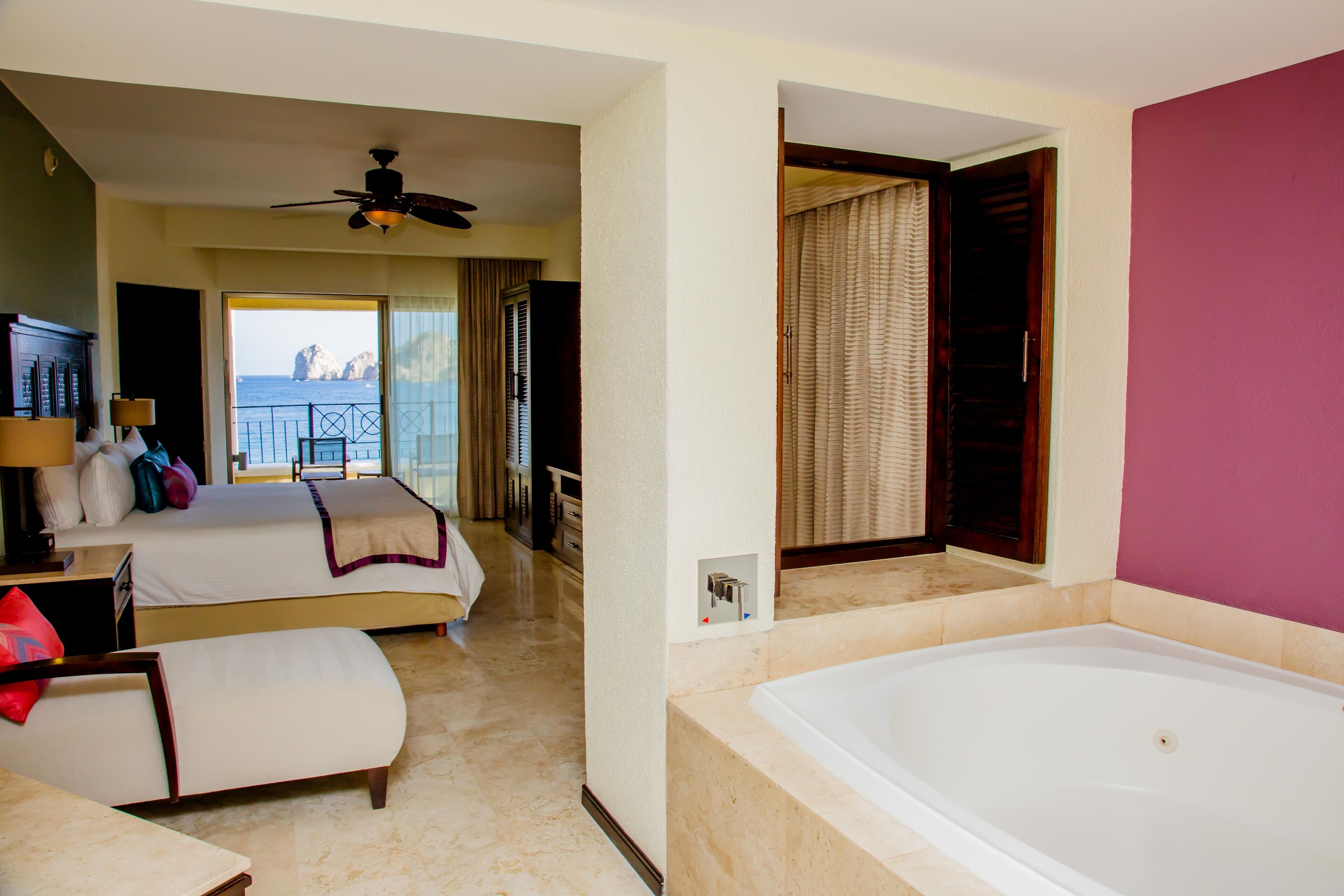A hotel room with two beds, a large bathtub, and a balcony with a view of the sea.