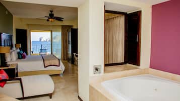 A hotel room with two beds, a large bathtub, and a balcony with a view of the sea.