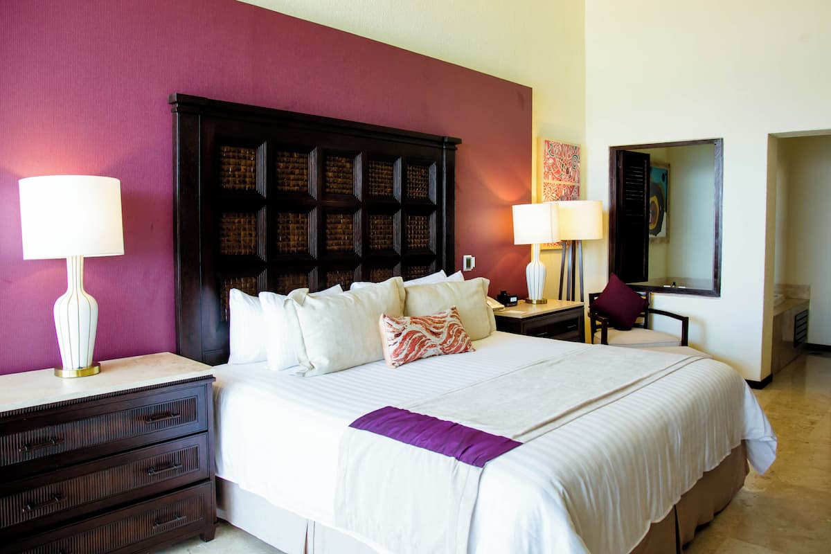 A hotel room with a large bed, two bedside tables with lamps, a nightstand, a chair, and a mirror.