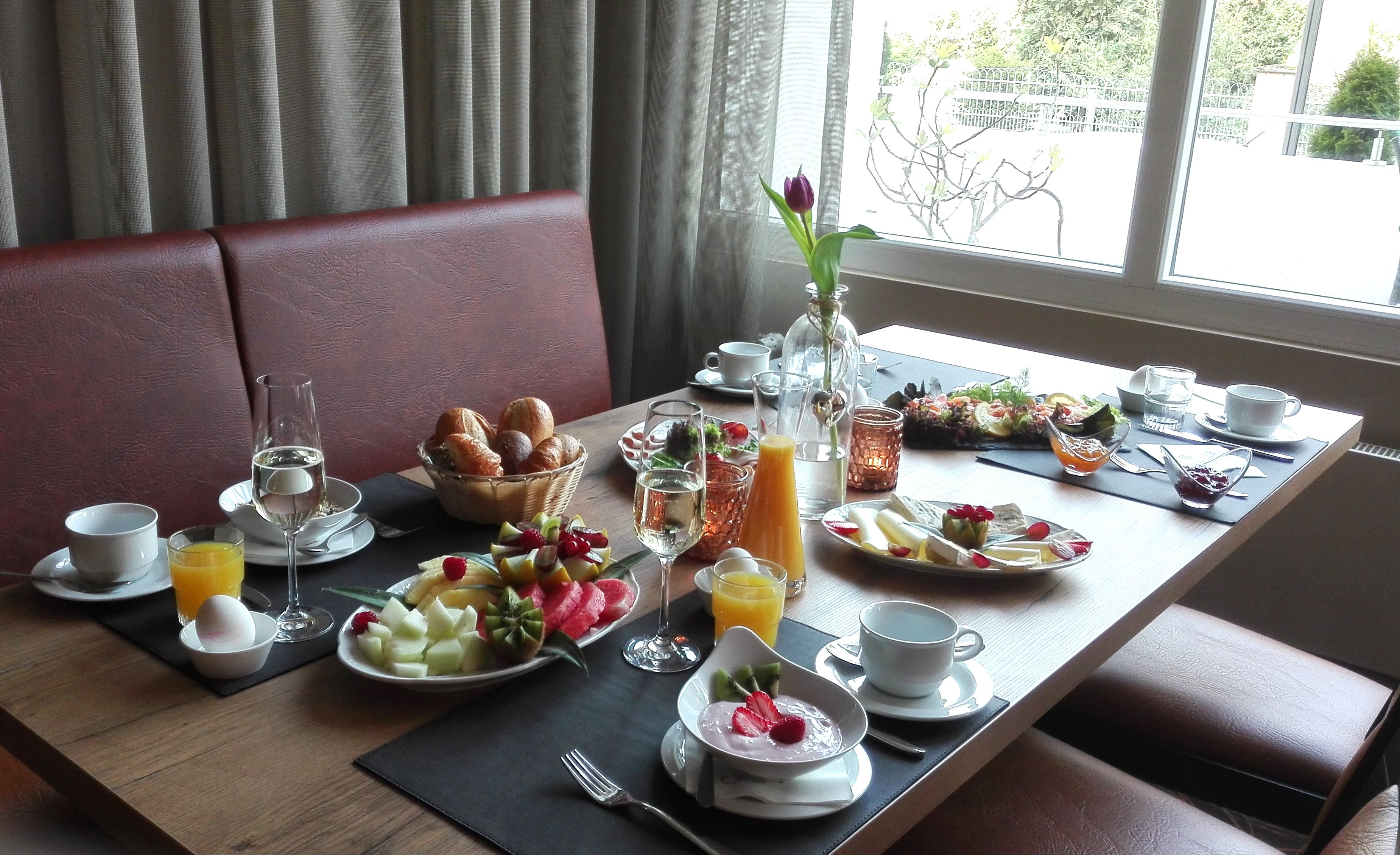 A breakfast setting with a variety of foods and beverages on a table, including fruits, pastries, and a glass of orange juice.