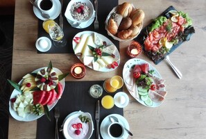 Una mesa de madera con una variedad de frutas, quesos, pan y bebidas para el desayuno.