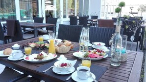 An outdoor dining area with tables set for breakfast, including plates of food, drinks, and a variety of fruits and pastries. - Caravelle Hotel im Park (Bad Kreuznach)