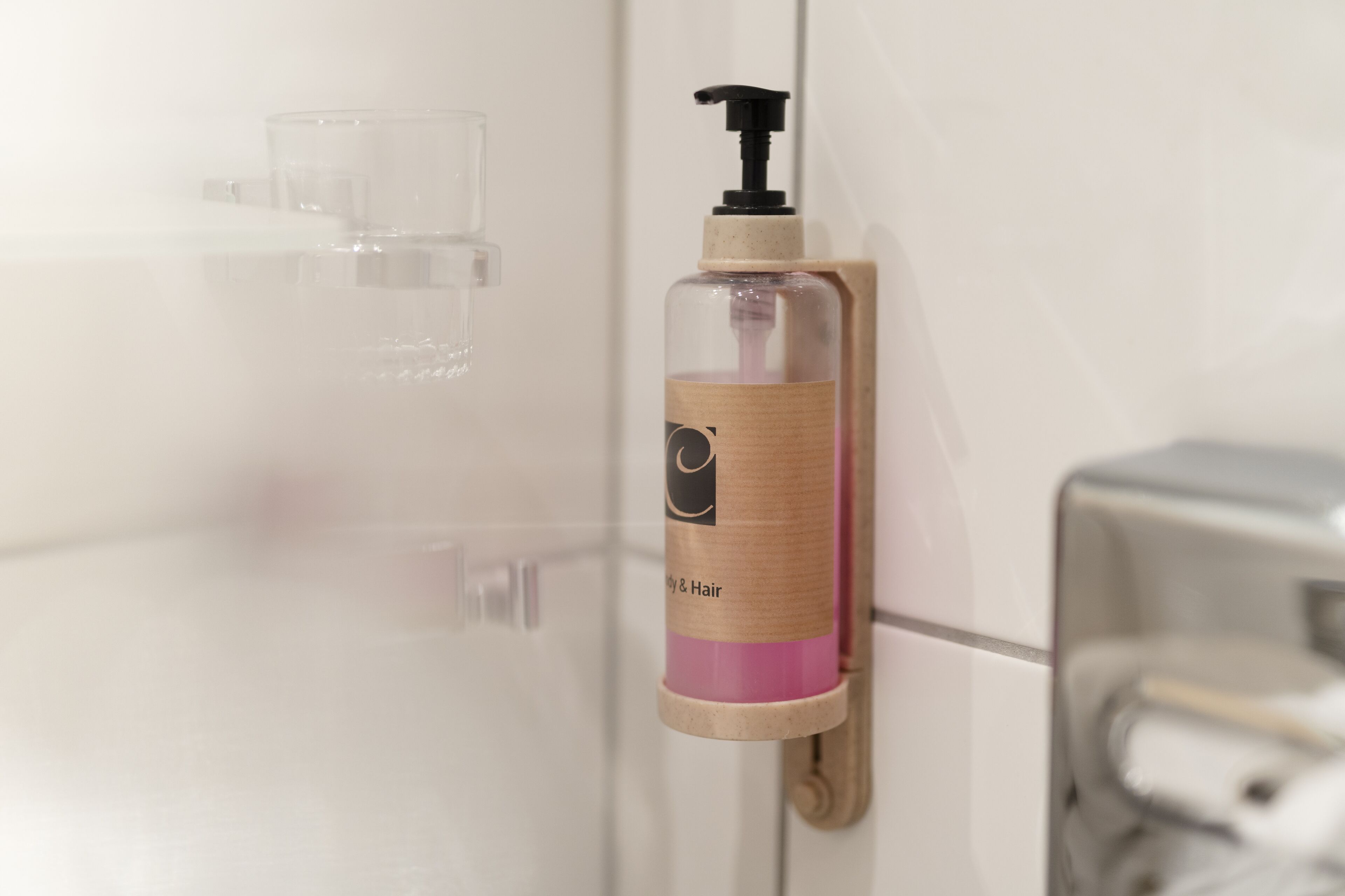 Ein Badezimmer mit einem klaren Glas-Seifenspender, der an einem beigen Handtuchhalter angebracht ist.