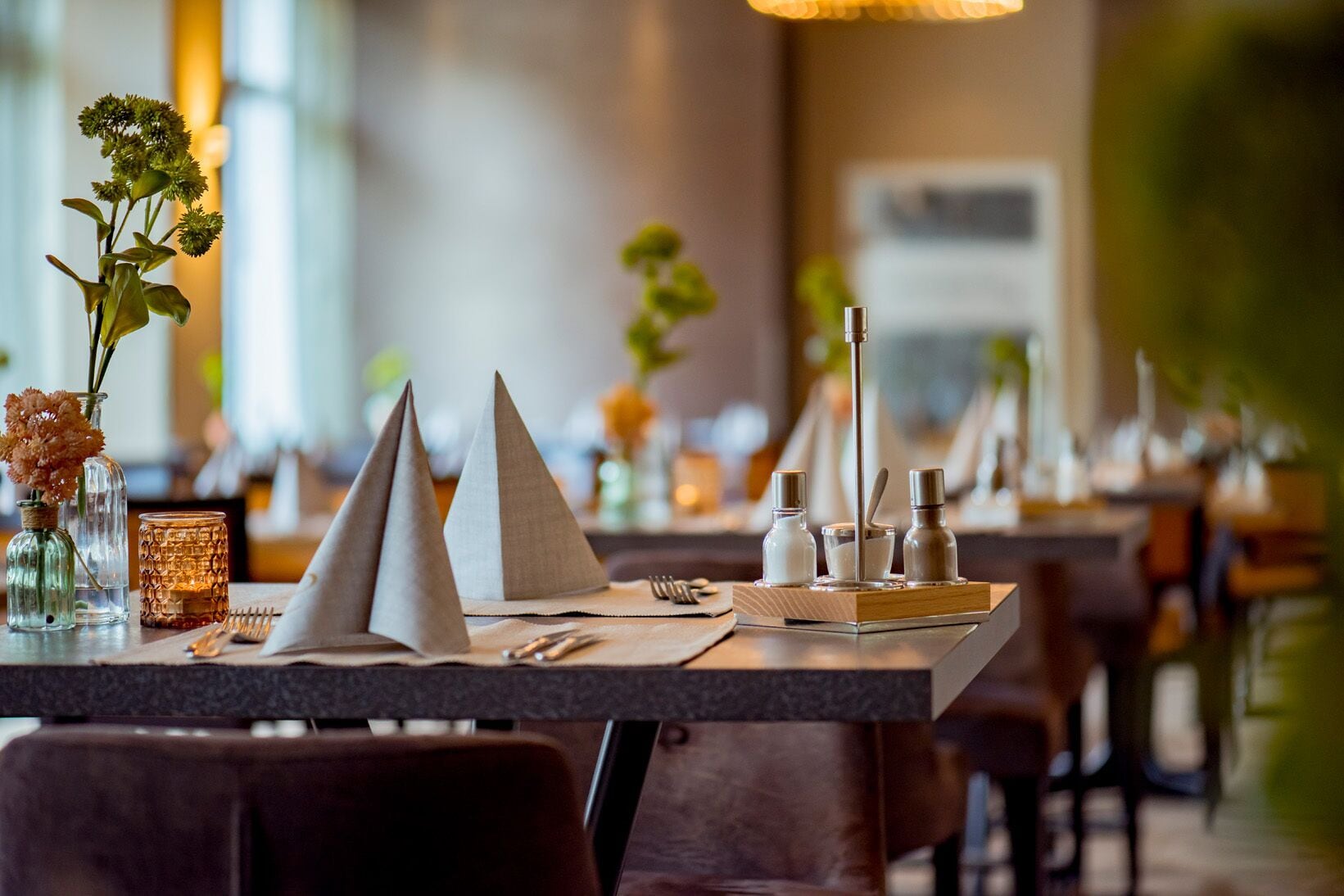 En restaurantscene med et dækket bord, inklusive en servietholder, salt- og peberkværn samt et stearinlys.