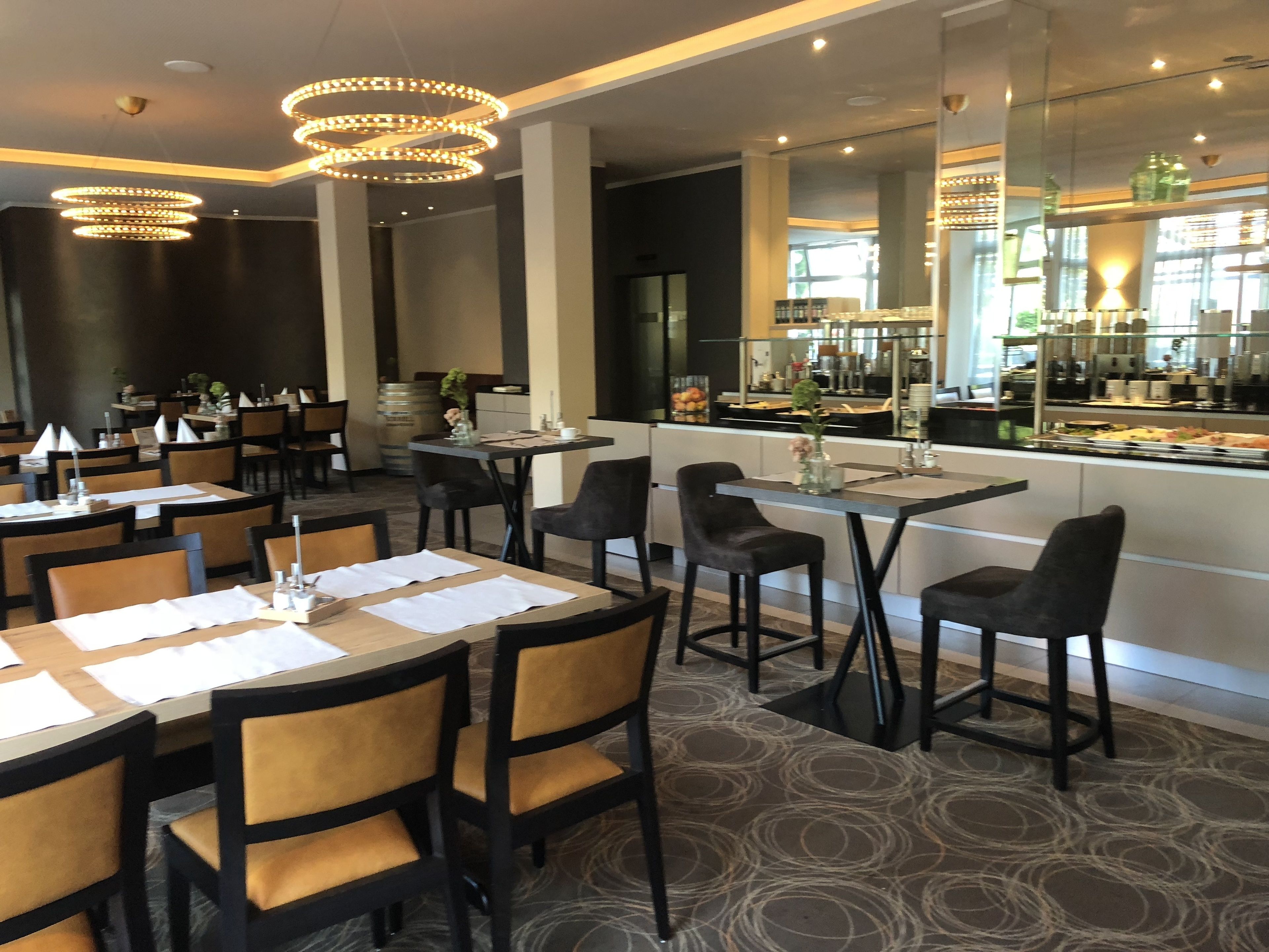 Un restaurante con varias mesas y sillas, una zona de bar y vistas a la cocina.