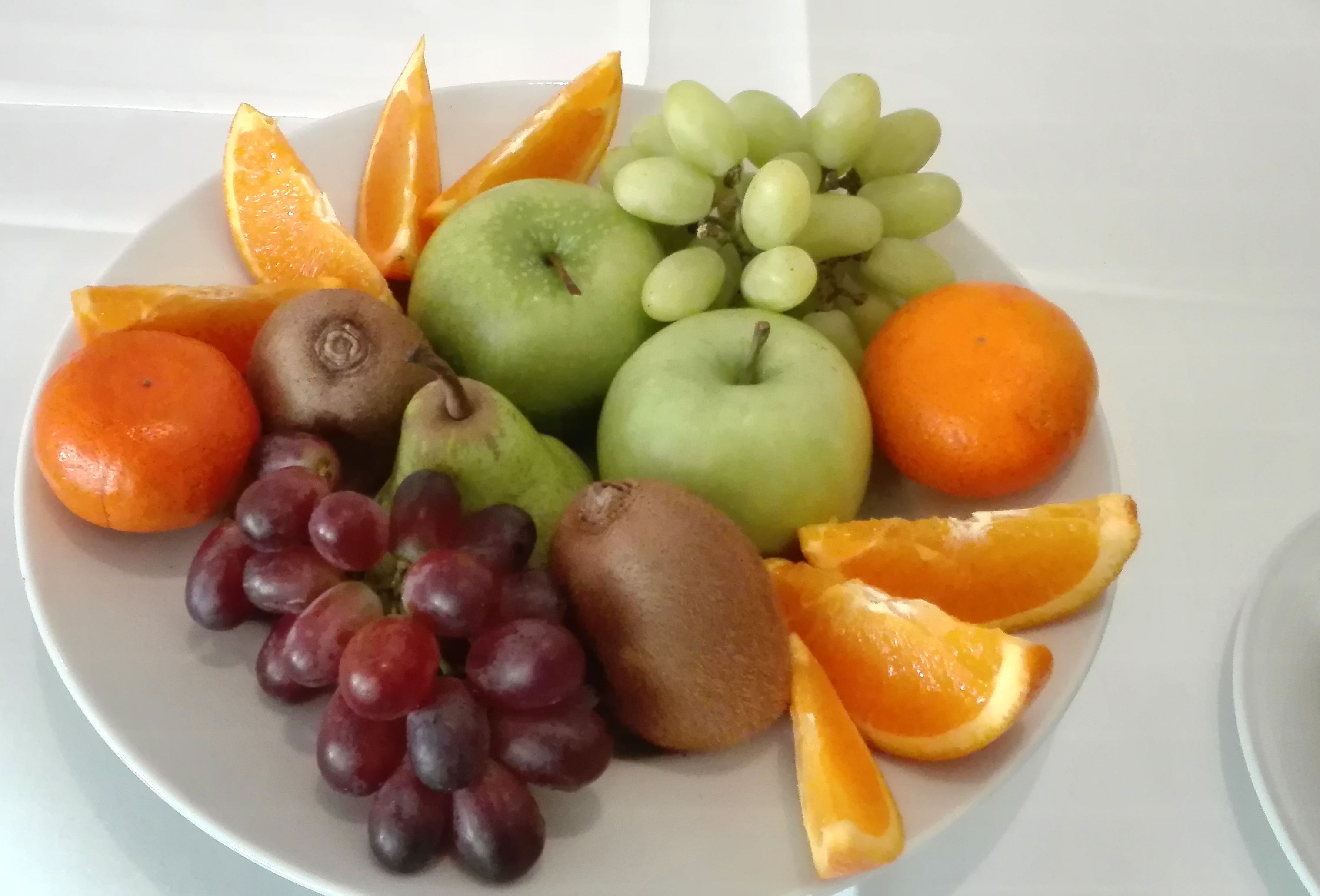 Une assiette contenant divers fruits, notamment des pommes, des oranges, des raisins et des kiwis.
