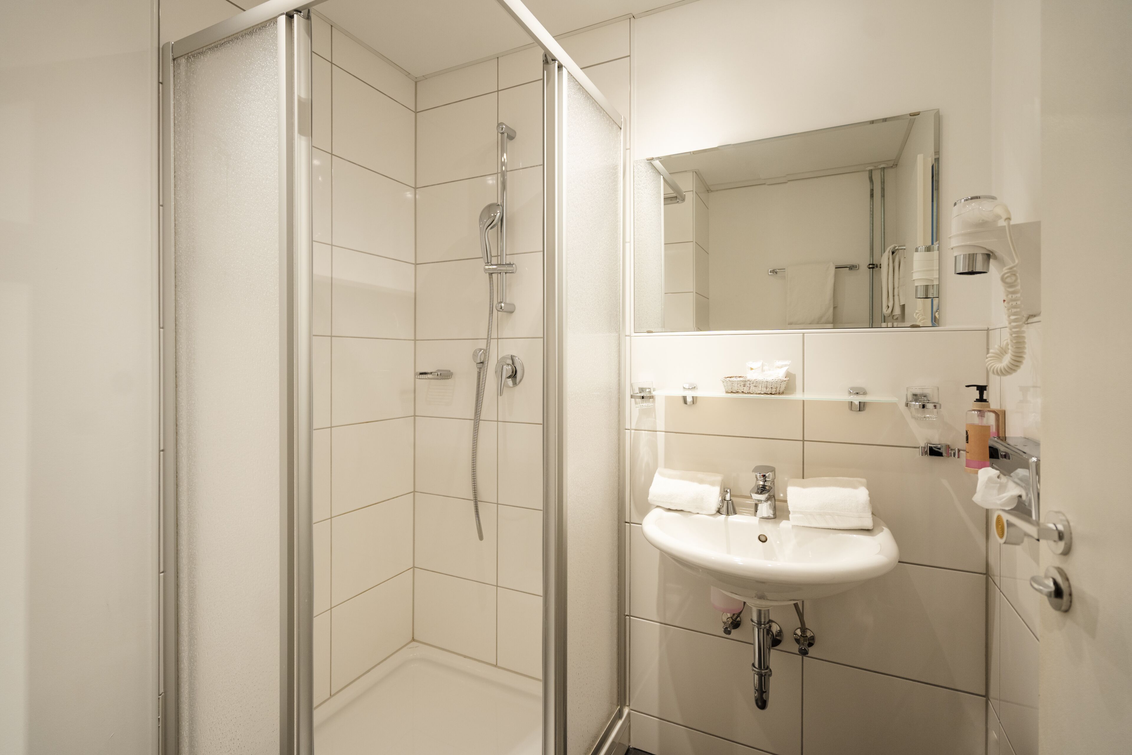 Une salle de bain moderne avec une douche à parois de verre, un lavabo blanc et un miroir au-dessus.