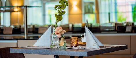 Une table à manger dressée avec un vase de fleurs, une bougie et un porte-serviettes.