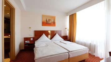 A hotel room with a double bed, a bedside table with a lamp, a painting on the wall, and a window with curtains.