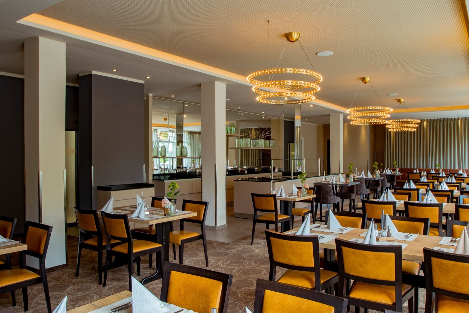 A spacious restaurant with multiple dining tables and chairs, a central bar area, and modern lighting fixtures.