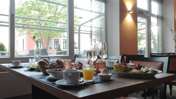A breakfast table set with various fruits, pastries, and beverages, with a view of trees and buildings outside. - Caravelle Hotel im Park (Bad Kreuznach)