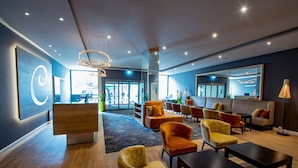 A modern lobby with a reception desk, seating area, and a large mirror. - Caravelle Hotel im Park (Bad Kreuznach)