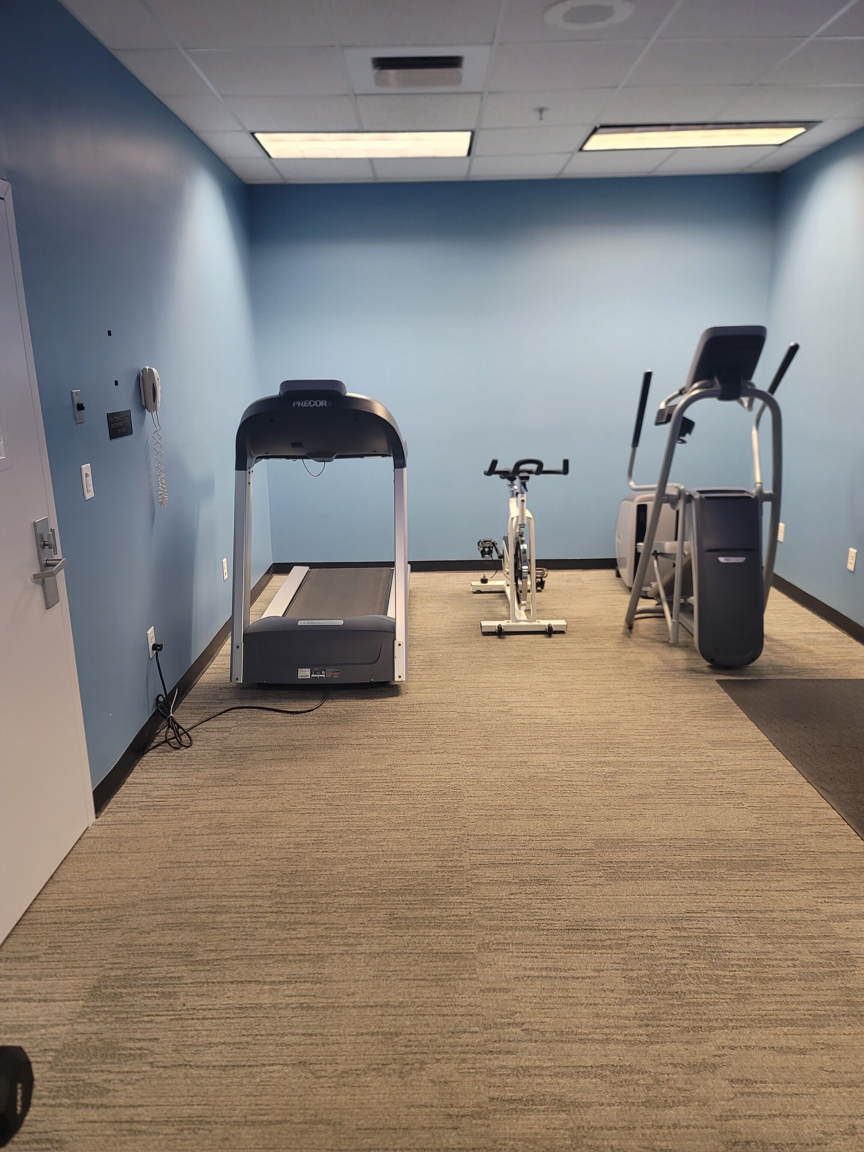 A room with a treadmill, stationary bike, and elliptical machine.