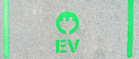 A parking sign with a green EV symbol and the letters "EV" on a textured asphalt surface.