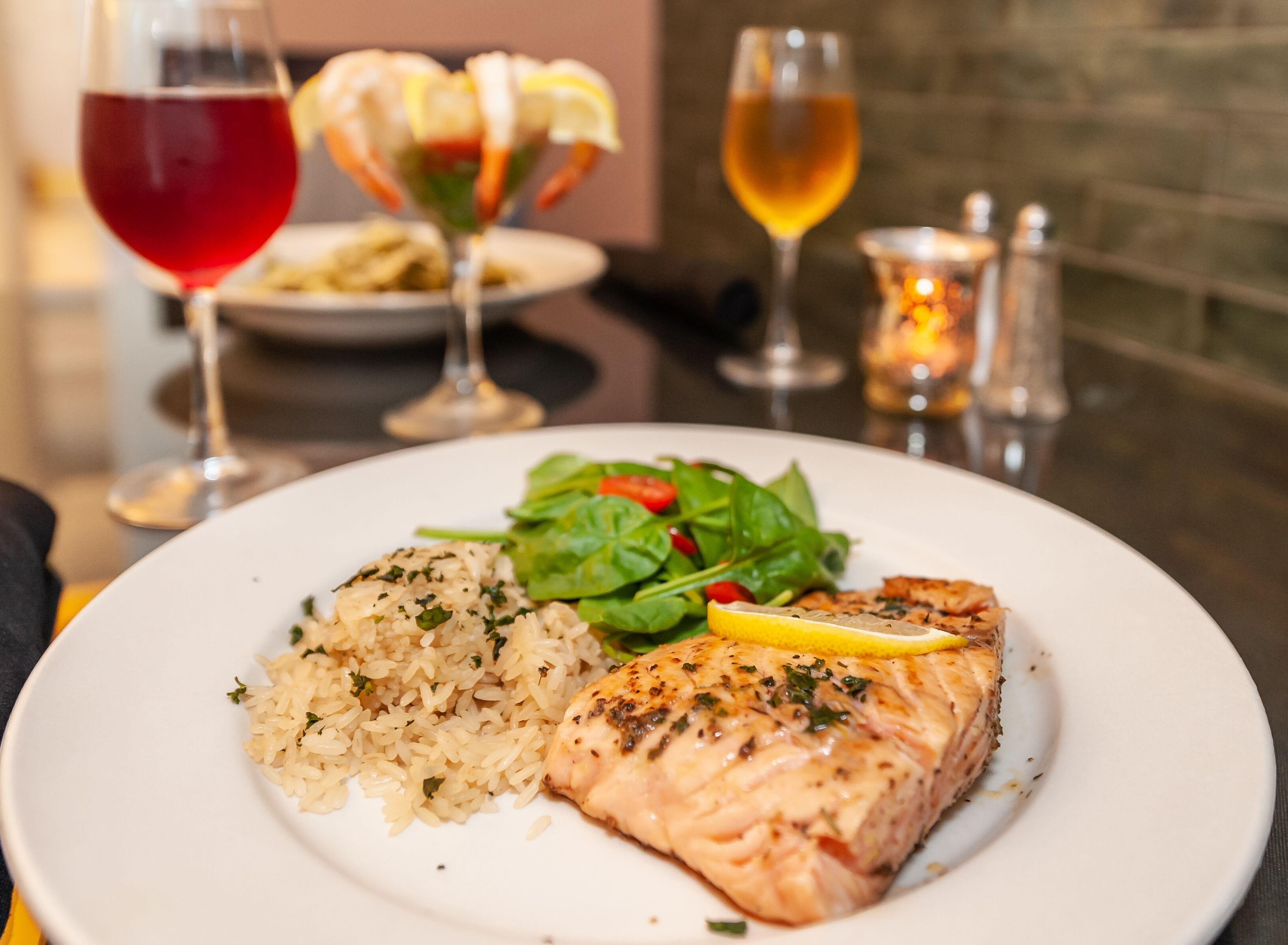 A plate of salmon, rice, and salad with a glass of red wine and a glass of white wine in the background.