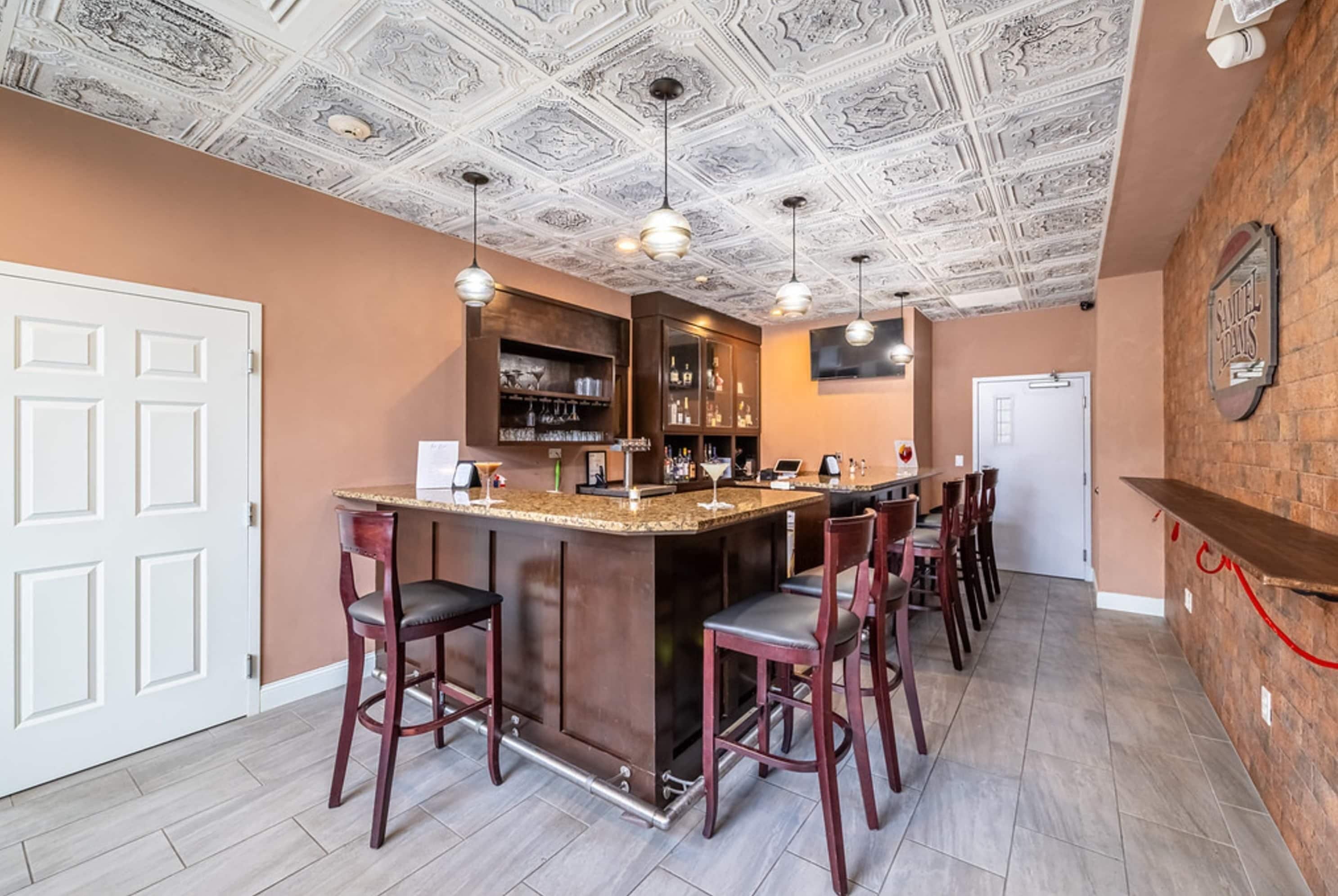 Zona de bar con mostrador de madera, taburetes y techo con diseños elaborados.
