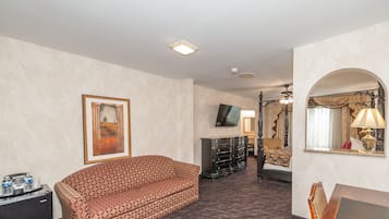 A hotel room with a patterned sofa, a TV, a dresser, a desk, and a mirror.
