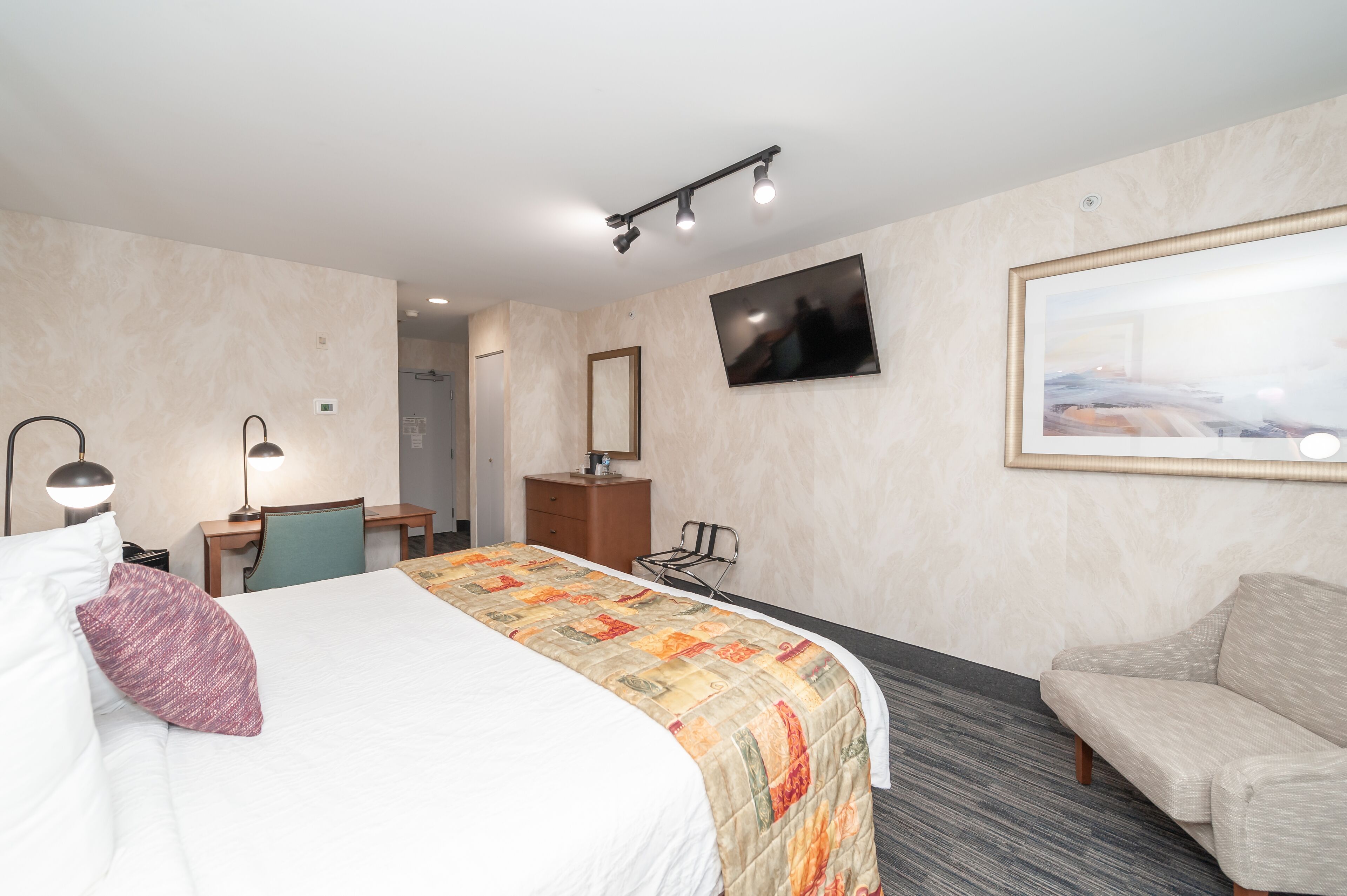 Une chambre d’hôtel avec un lit, un bureau, une chaise, une télévision et un canapé.