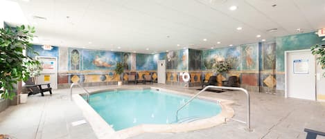 Uma piscina interna com piso em azulejo, cadeiras de descanso e um mural nas paredes.