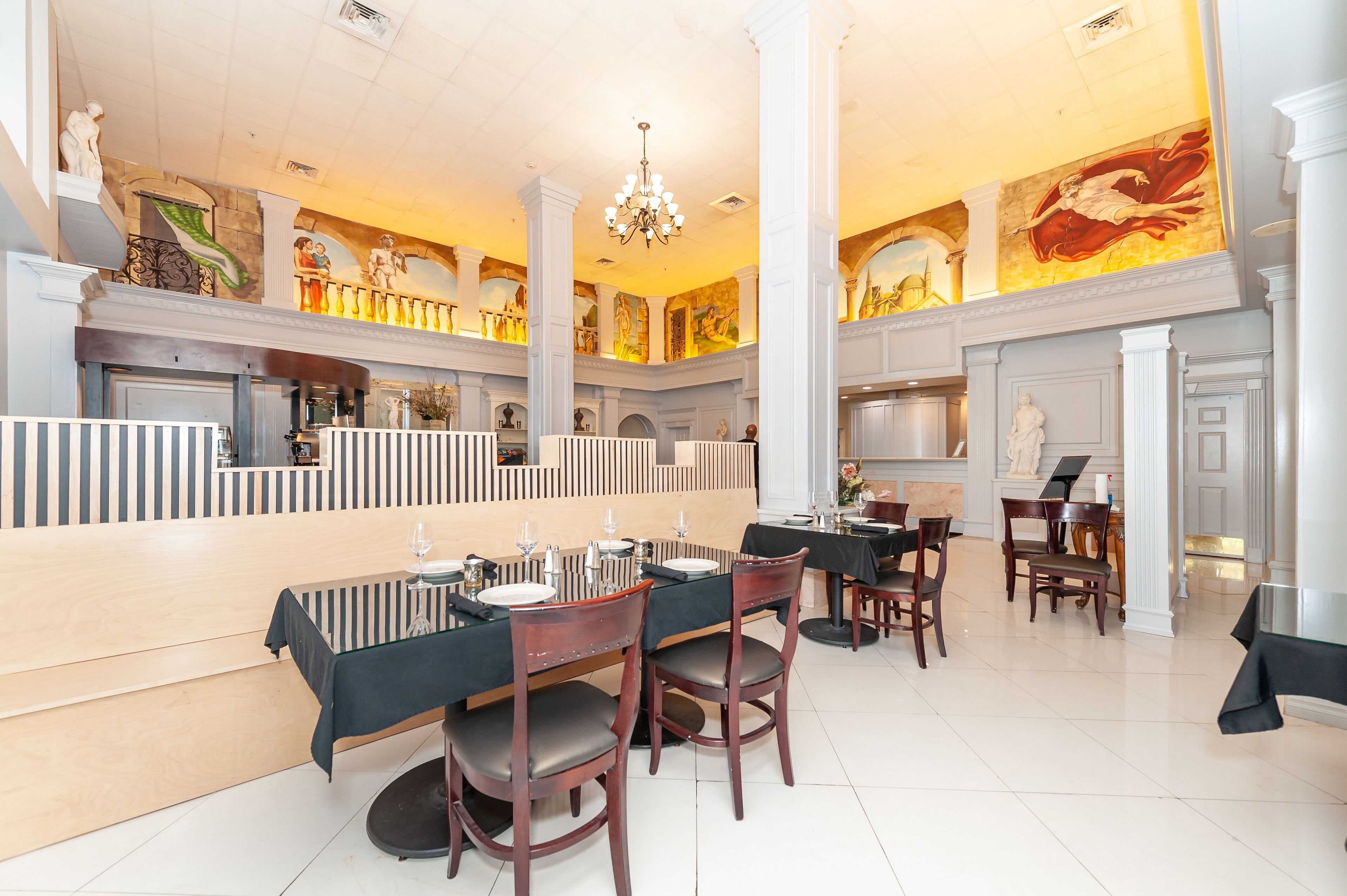 A spacious dining area with high ceilings, ornate columns, and a chandelier.