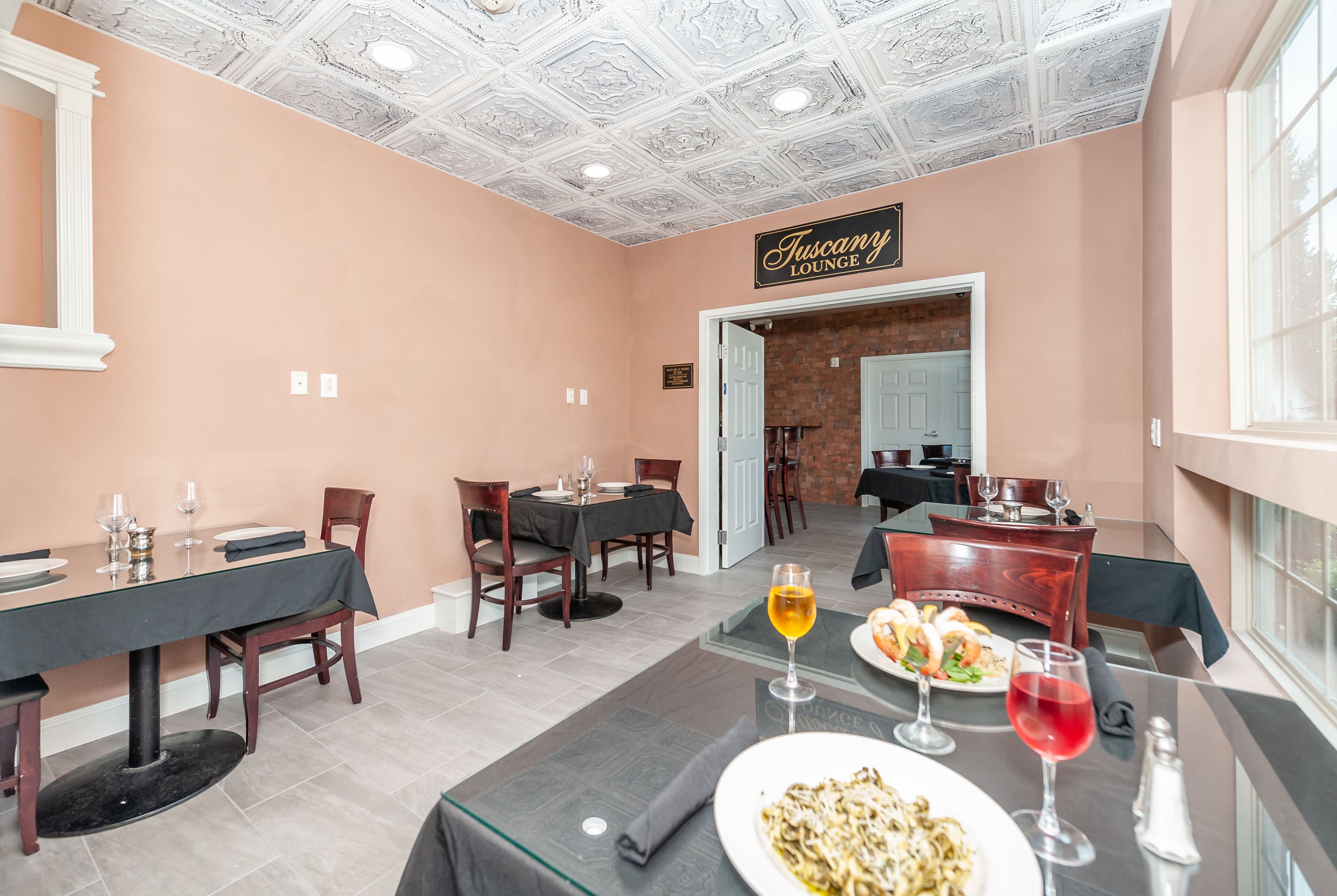 A restaurant with peach-colored walls, a 'Tuscan Lounge' sign, and tables set with plates and glasses.