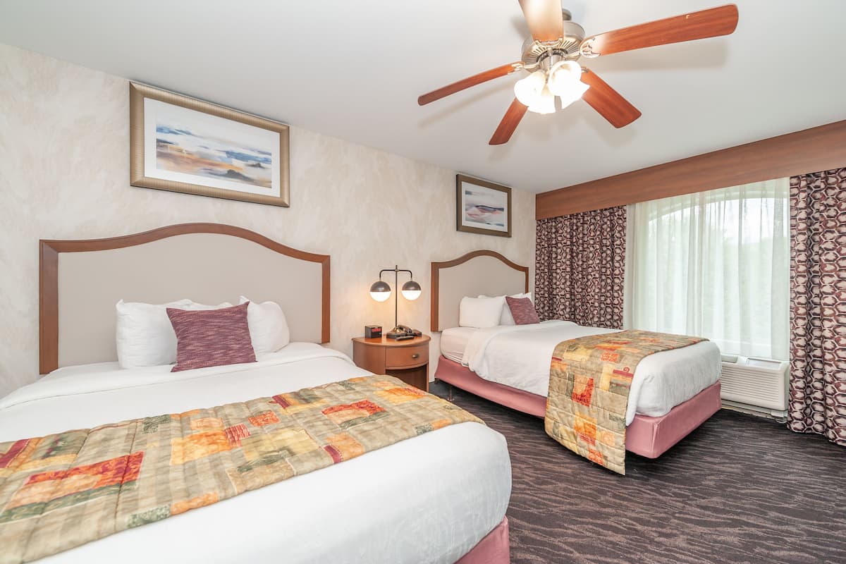 A hotel room with two beds, a ceiling fan, and a large window with curtains.