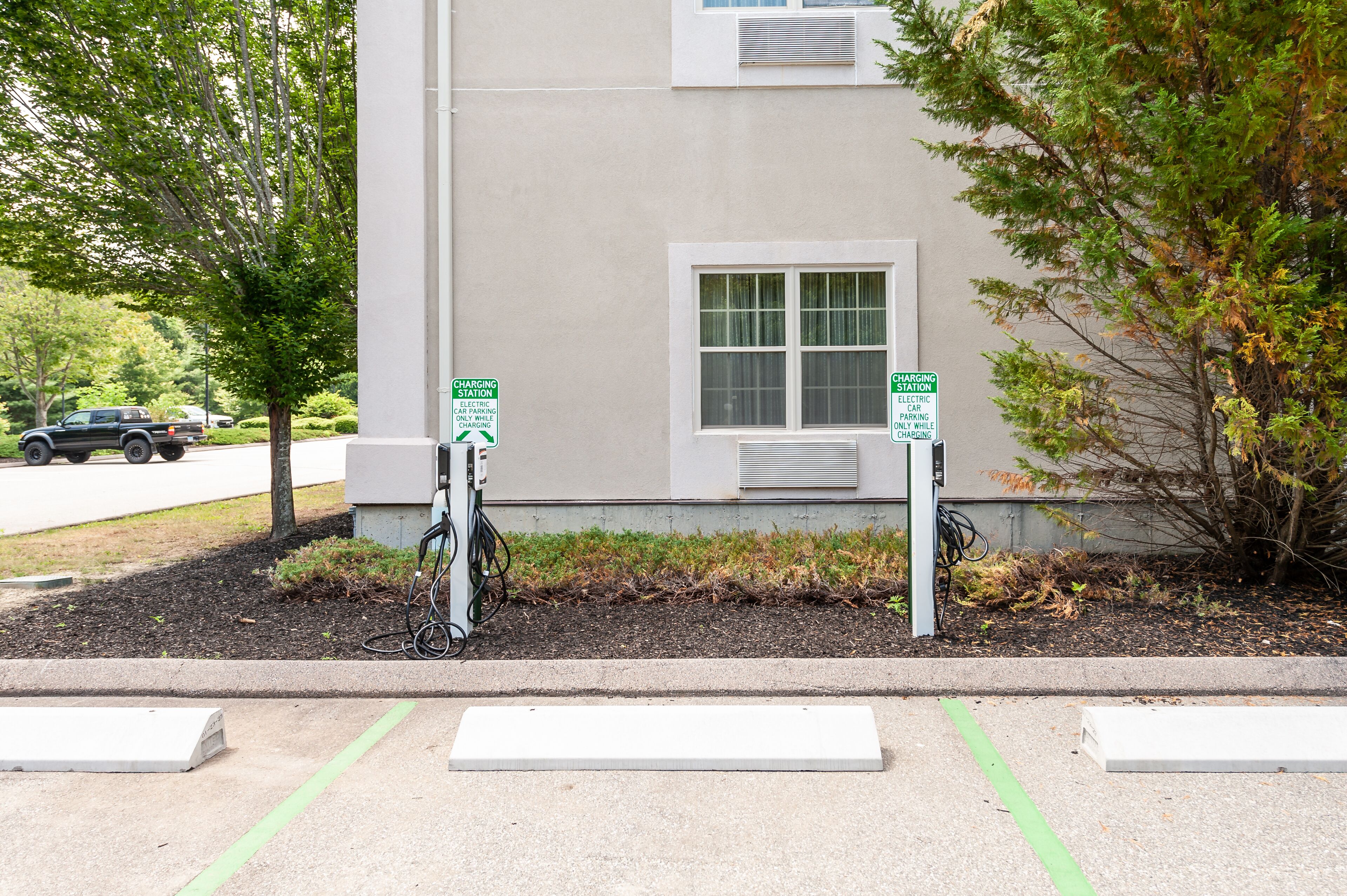 A building with two charging stations for electric vehicles, a window, and a sidewalk with a curb.