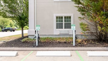 A building with two charging stations for electric vehicles, a window, and a sidewalk with a curb.