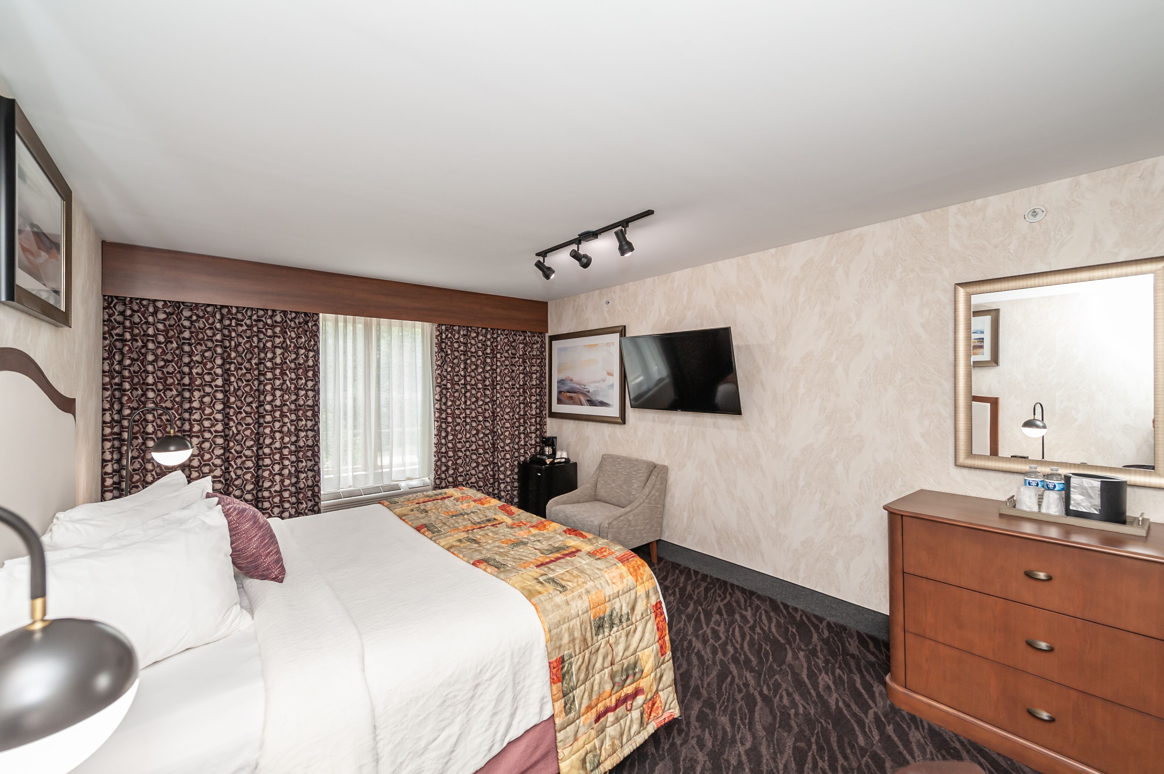 Habitación de hotel con cama, escritorio, silla, cómoda y televisión.