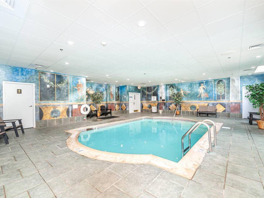 Una piscina interior con suelo de baldosas, bancos y un mural en las paredes.