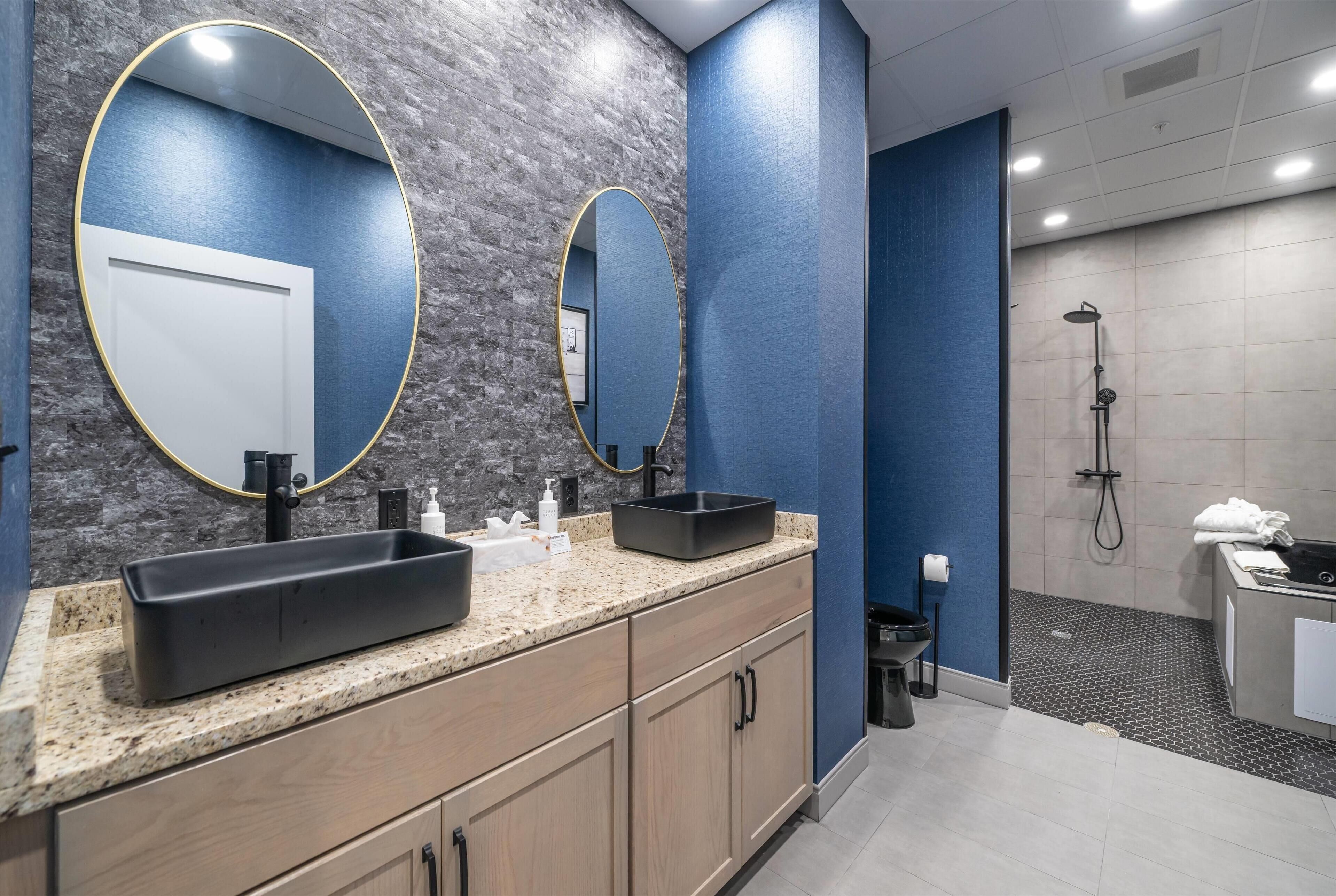 Une salle de bain moderne avec un comptoir en granit, deux lavabos, un grand miroir et un espace douche.