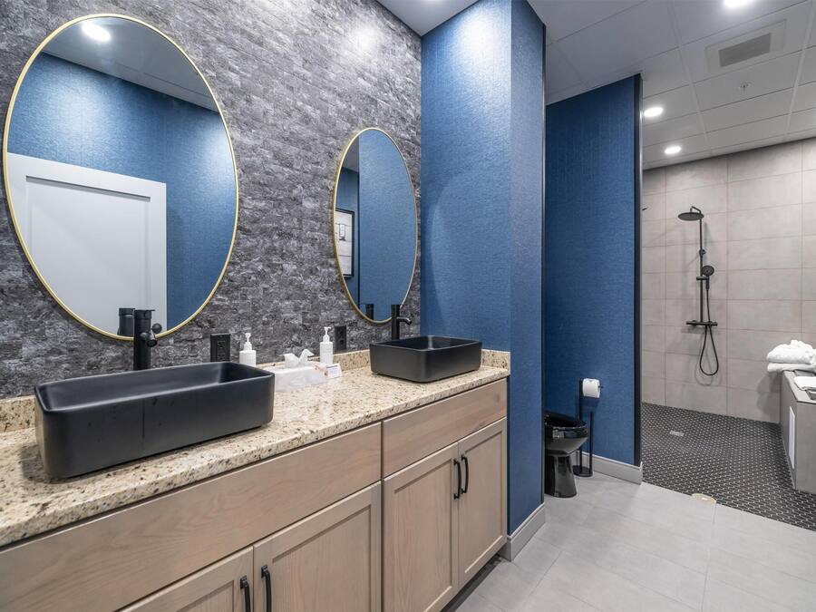 A modern bathroom with a granite countertop, two sinks, a large mirror, and a shower area.