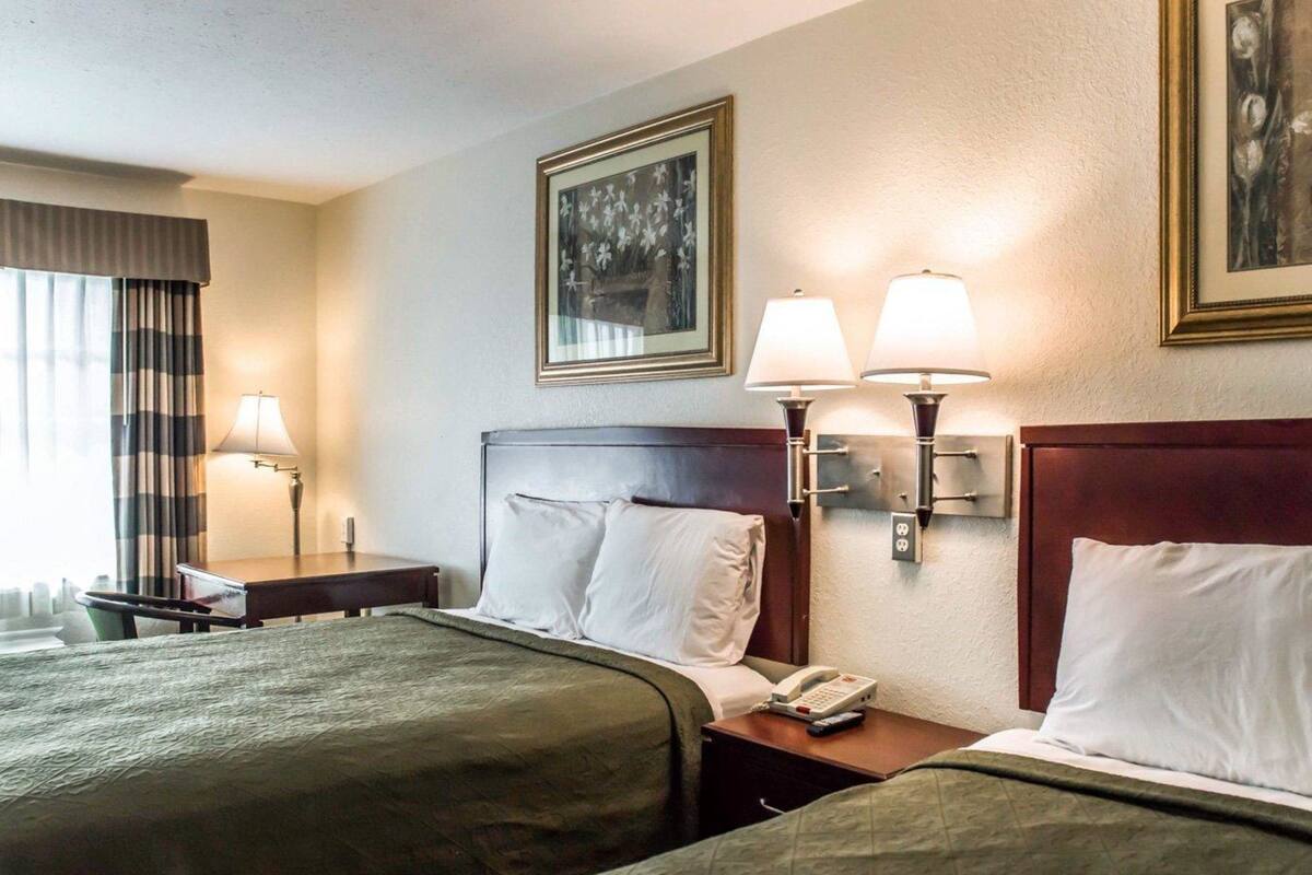A hotel room with two beds, a nightstand with a phone, two wall-mounted lamps, and a painting on the wall.