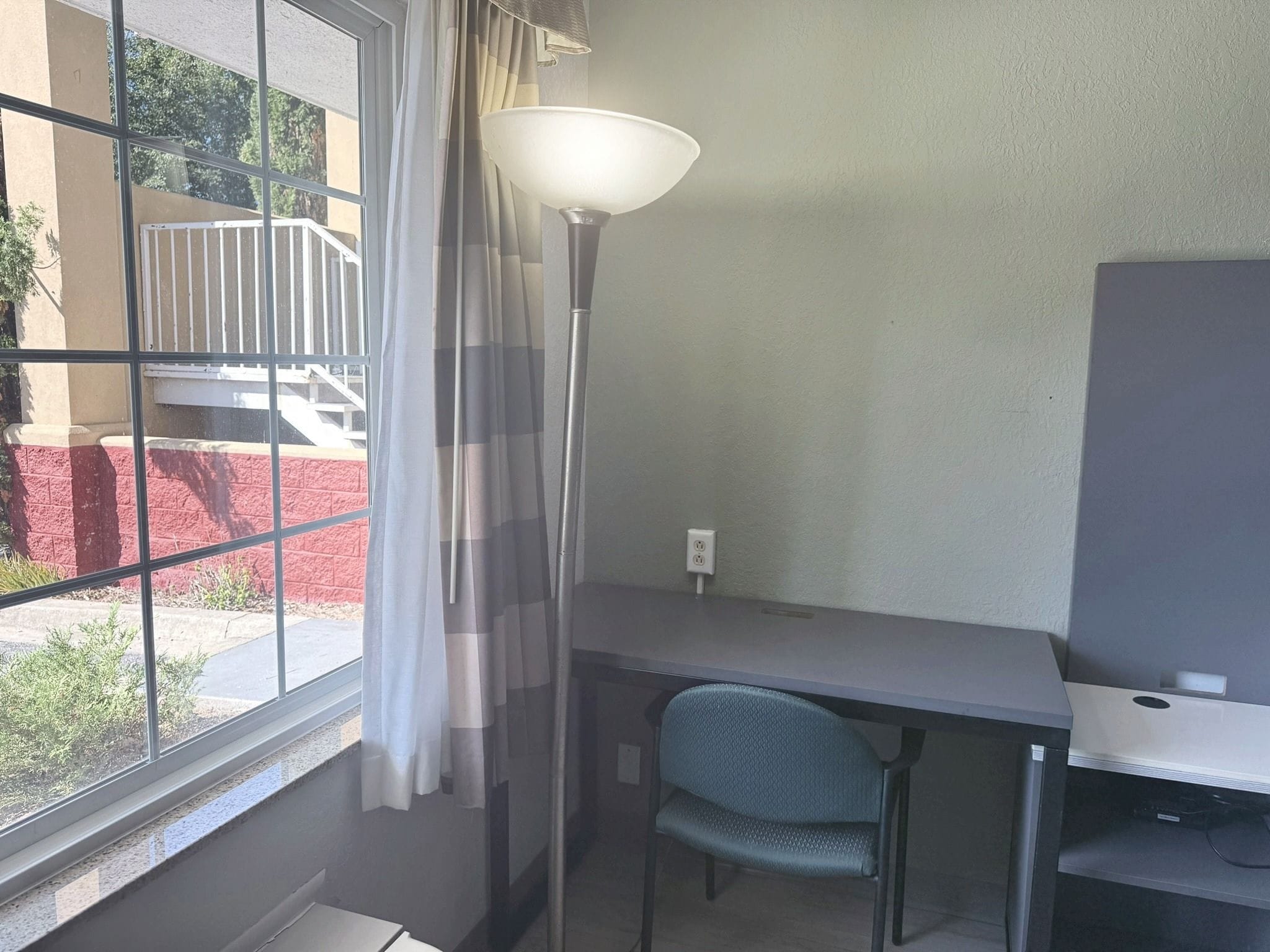 Una habitación con escritorio, silla y un amplio ventanal con cortinas.