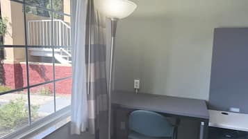 Una habitación con escritorio, silla y un amplio ventanal con cortinas.