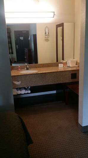 Un baño de hotel con lavamanos, espejo, dispensador de toallas y un perchero para toallas.