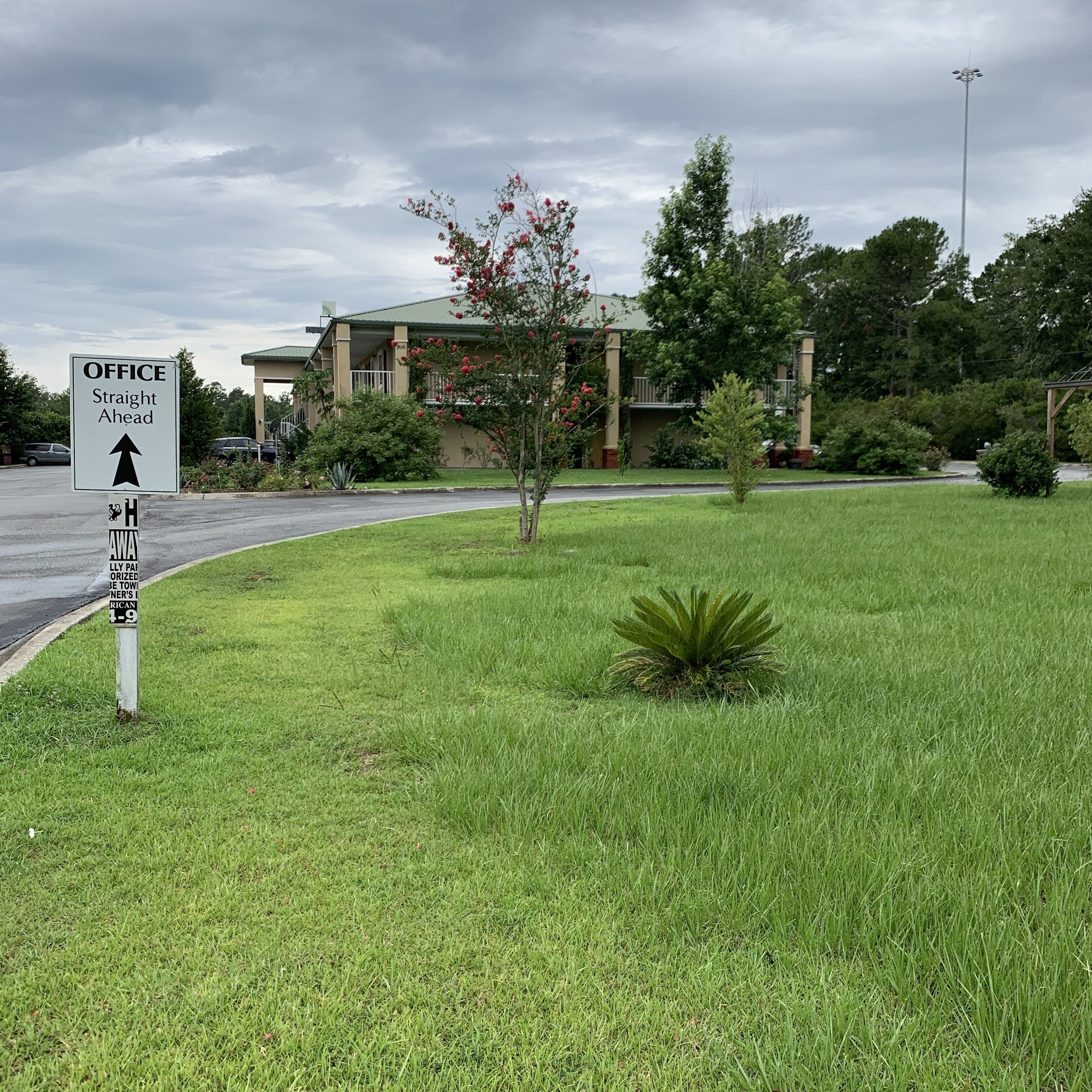 Un panneau indiquant la direction d’un bureau, situé juste devant, entouré d’une zone herbeuse avec un bâtiment en arrière-plan.