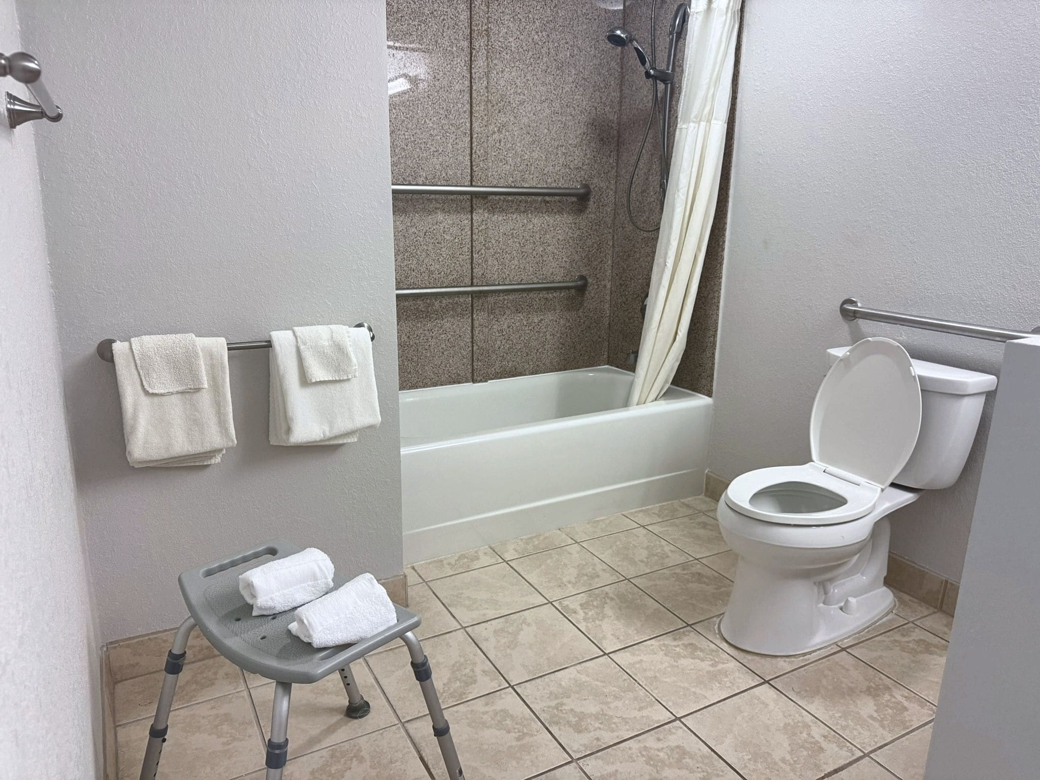 A bathroom with a toilet, a shower, and a bathtub. There are two towels hanging on a rack.
