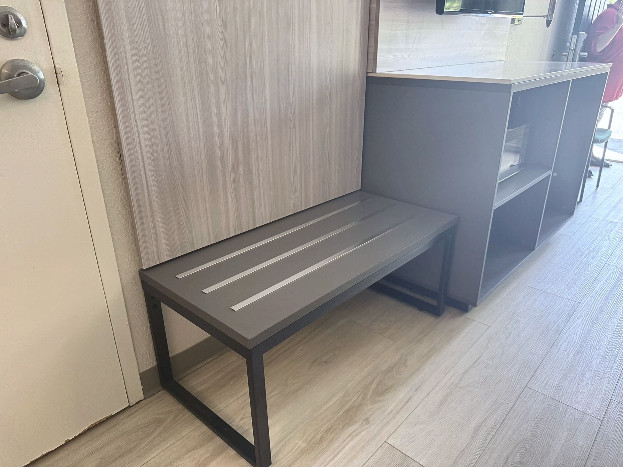 Un banc doté d’une structure métallique et d’une assise à lattes, placé à côté d’une porte et d’un comptoir.